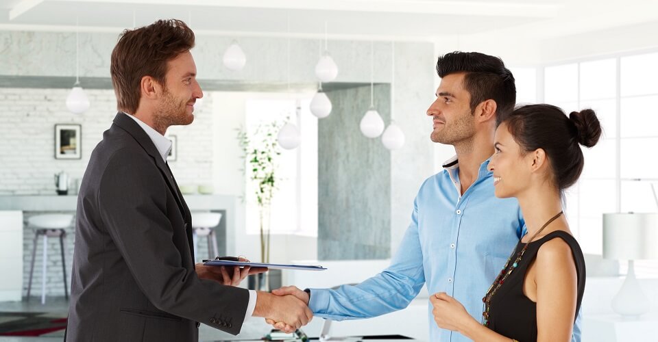 Young couple and real estate agent shaking hands, smiling. Side view.