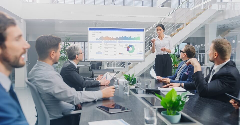 In the Corporate Meeting Room: Female Analyst Uses Digital Interactive Whiteboard for Presentation to a Board of Executives, Lawyers, Investors. Screen Shows Company Growth Data with Graphs