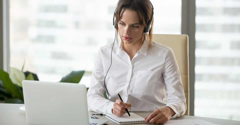 Serious businesswoman in headphones watching webinar on laptop making notes, learning studying computer course, making call, participating online conference, interpreter translating training class